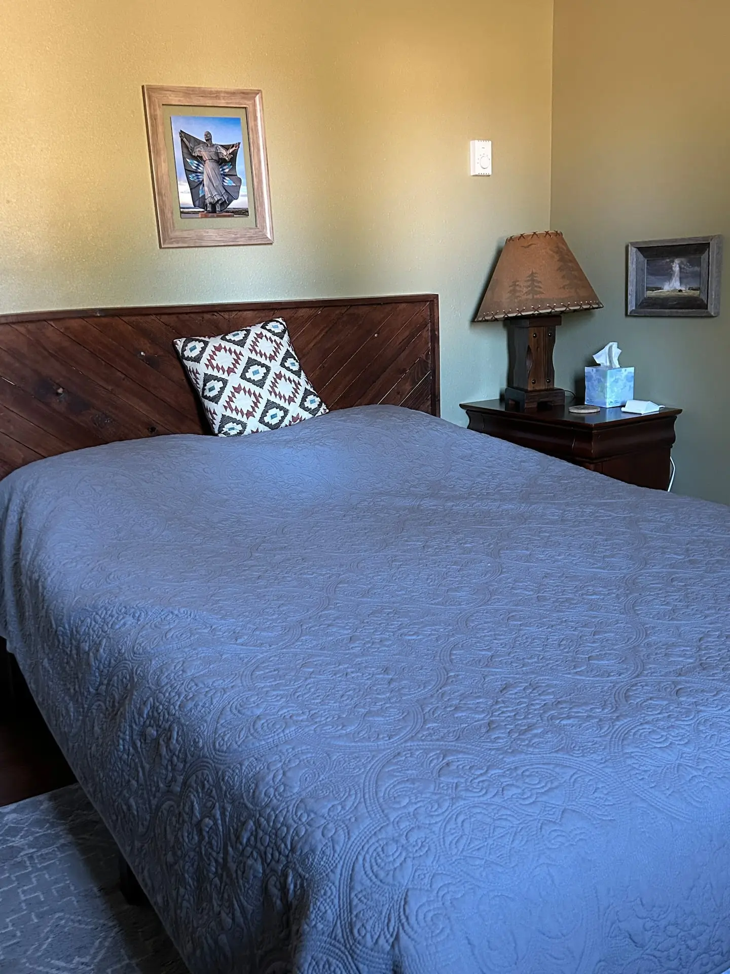 A bed with a blue quilt, carved wooden headboard and a table lamp in the second bedroom