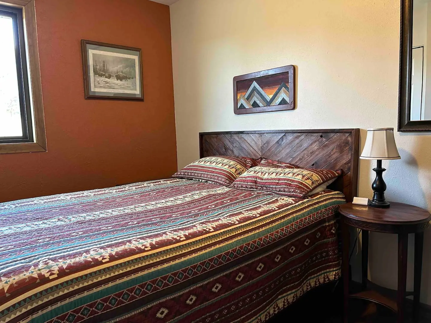 Queen bedroom with a Southwestern-patterned quilt, rust-colored accent wall and mountain artwork