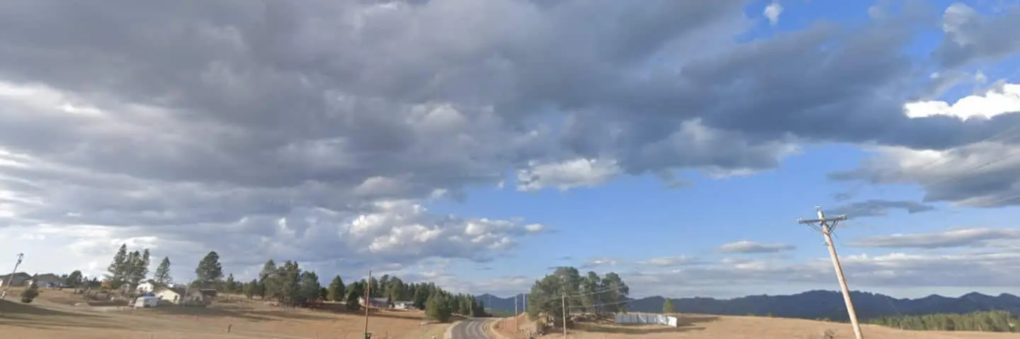 A wide panorama of rolling grassland and ponderosa pines under a cloudy South Dakota sky