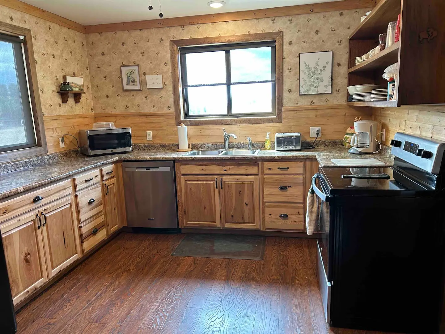 Full kitchen with oak cabinets, granite counters, dishwasher, electric range, microwave and coffee maker under a window with a hill view