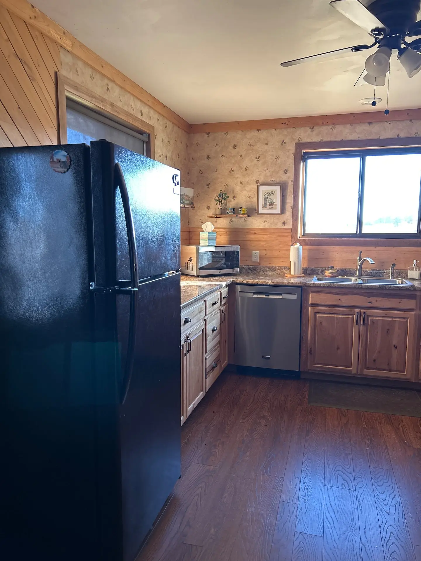 The kitchen's black refrigerator and wooden cabinets, with a window over the sink