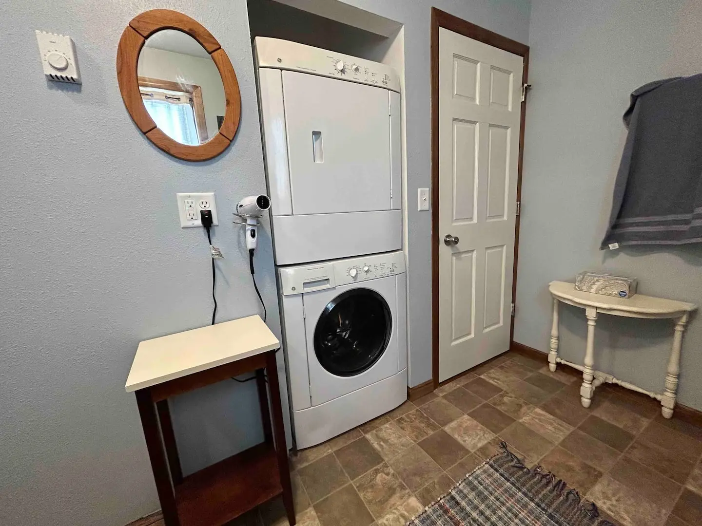 Laundry area with a stacked washer and dryer, a round mirror and a hair dryer