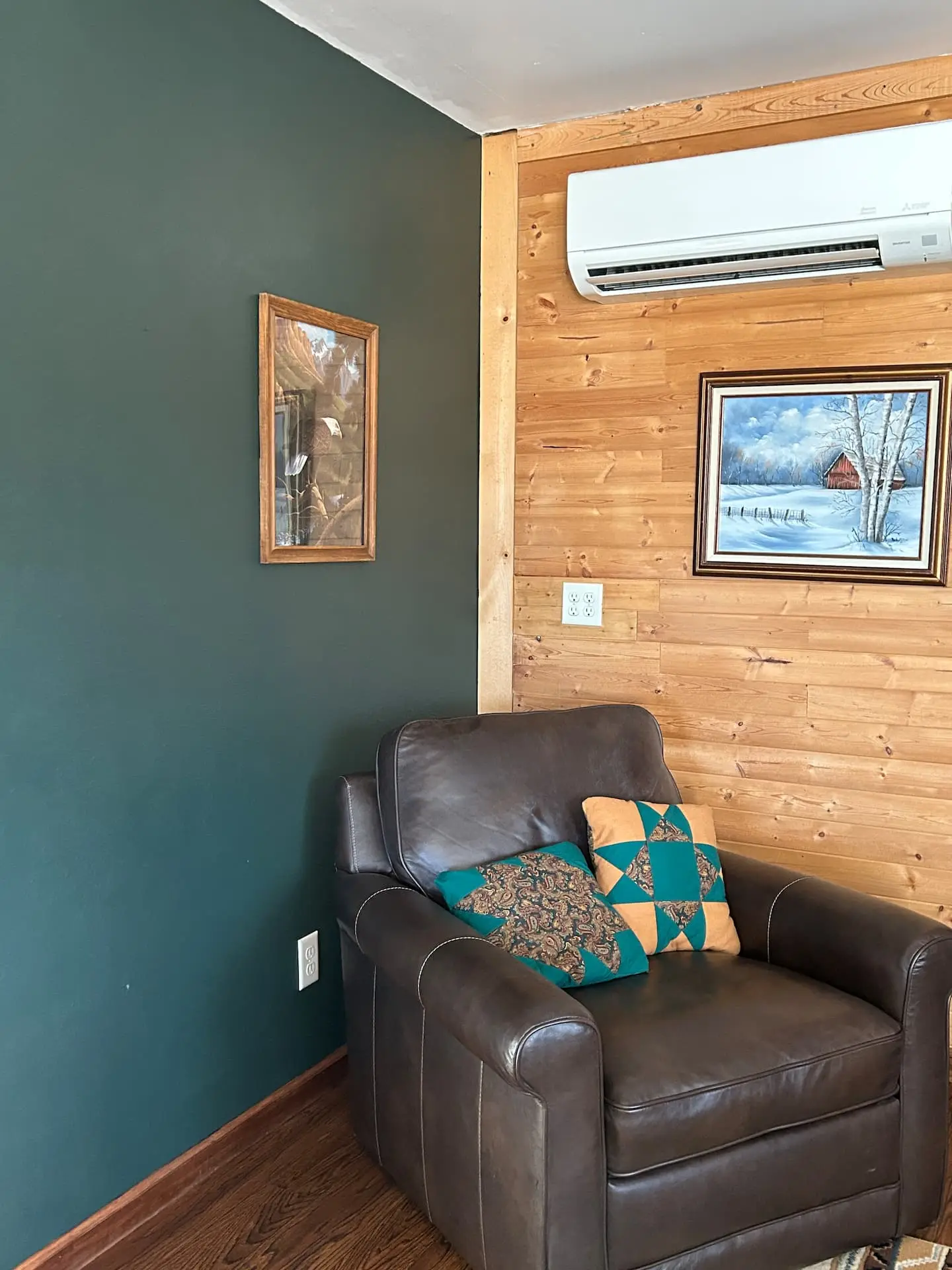 A leather armchair with Southwestern pillows in a corner of the living room, beside a teal accent wall and the wall-mounted air conditioner