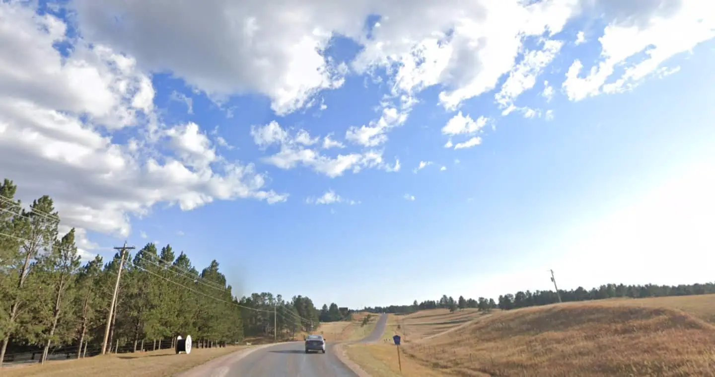 A wide view across the open grassland from the county road, under big clouds with the Black Hills beyond