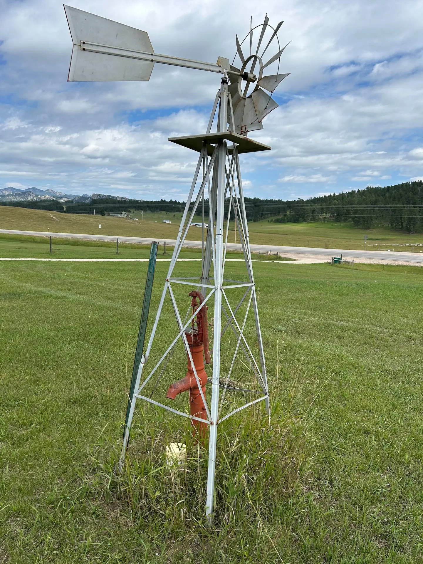 A white windmill standing in the green grass of the meadow, with the hills behind